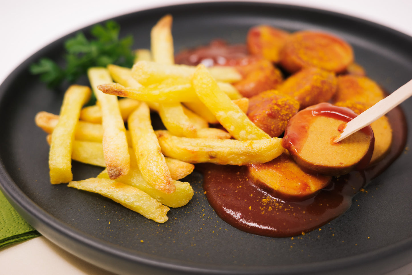 Currywurst aufgeschnitten auf einen Teller in Ketchup und Pommes dazu.