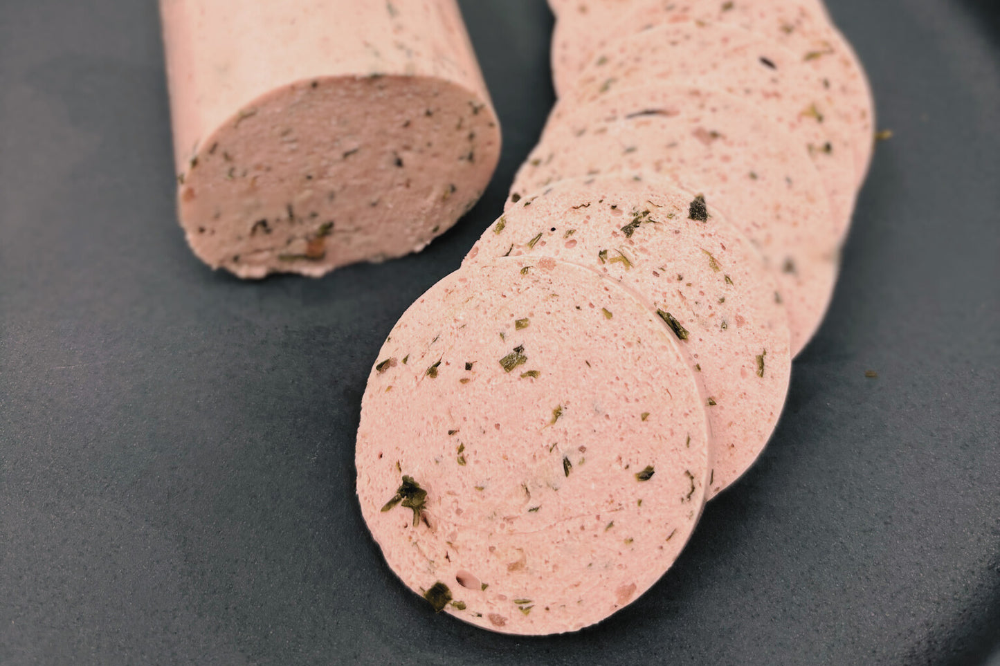 Veganer Lyoner mit Kräuter und Röstzwiebeln in Scheiben aufgeschnitten.