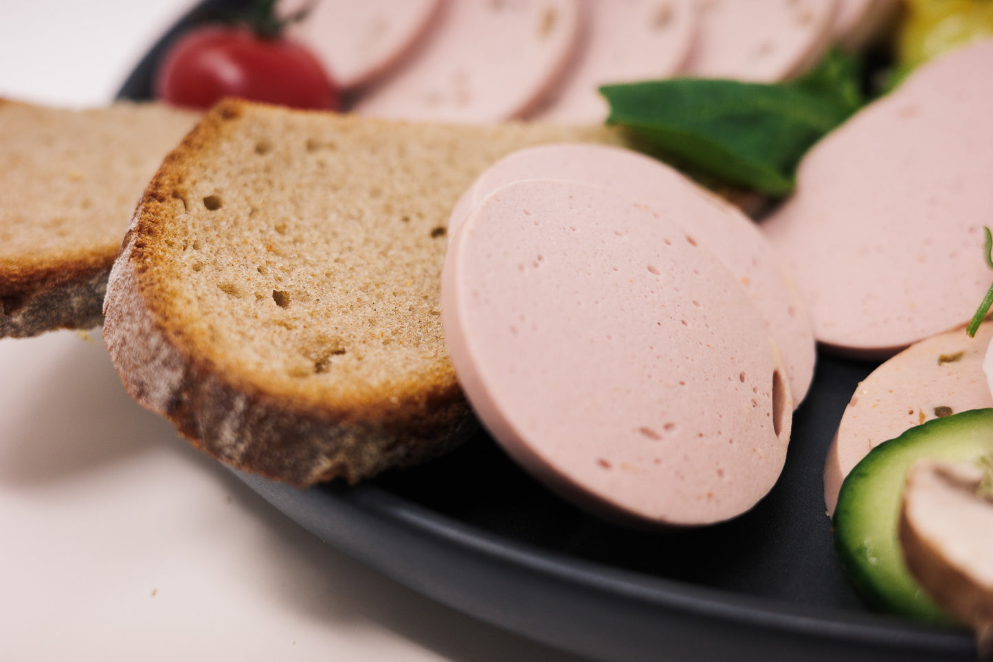Der vegane Lyoner natur aufgeschnitten serviert auf einen Teller mit einer Scheibe Brot.