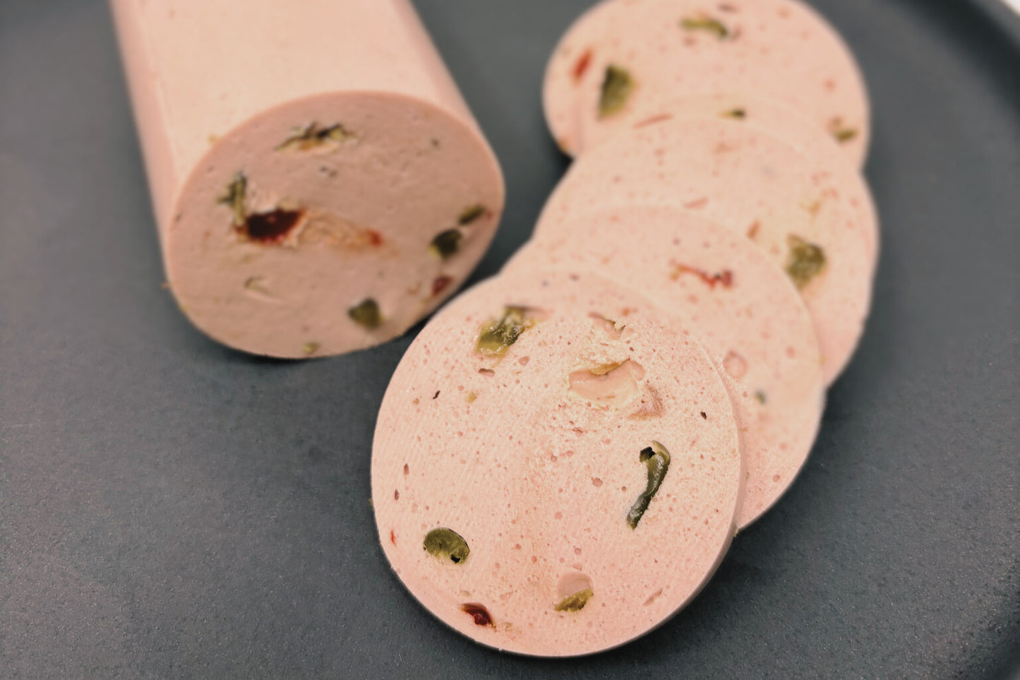 Unser veganer Paprika Lyoner zum Teil aufgeschnitten, man sieht die roten und grünen Paprikastücke.